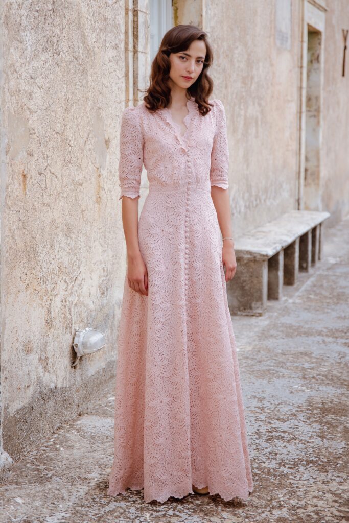 A fitted pink lace dress with long sleeves and a collared neckline, featuring a maxi length and button detailing.