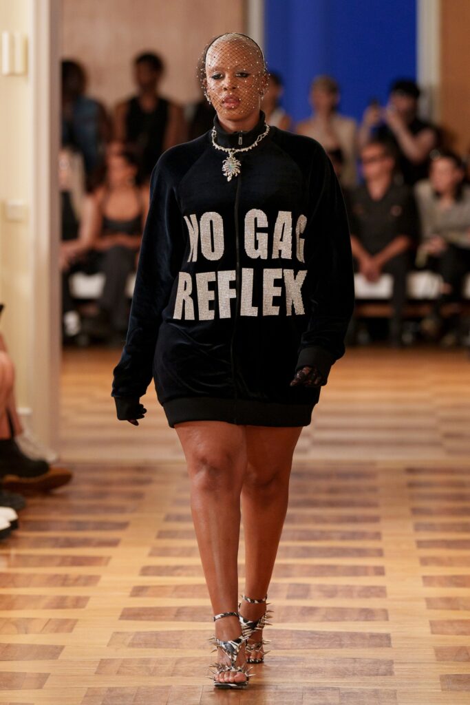 An oversized black cotton long-sleeve dress featuring bold text and a relaxed fit.