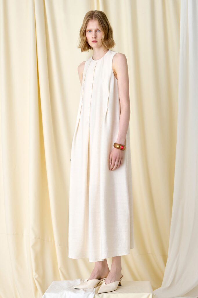 A relaxed cream cotton sleeveless dress with a high neckline and pleated maxi silhouette.