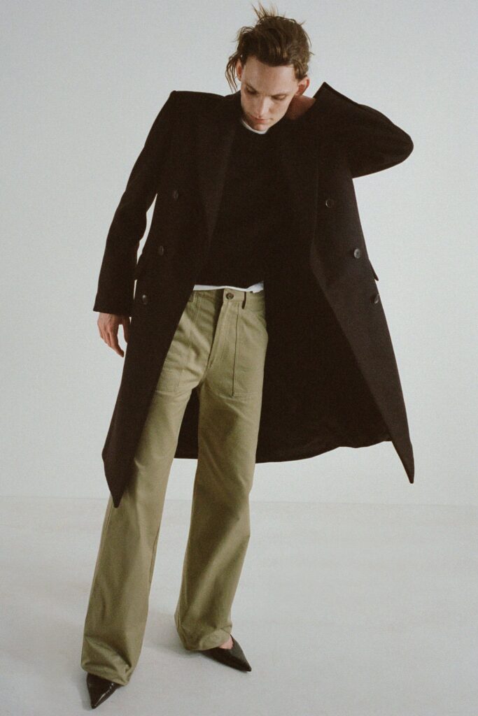A relaxed black coat paired with straight-leg green pants and a long-sleeve top.