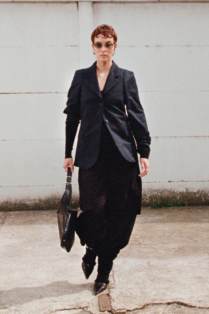 A fitted black blazer dress with long sleeves and an asymmetric design detail.