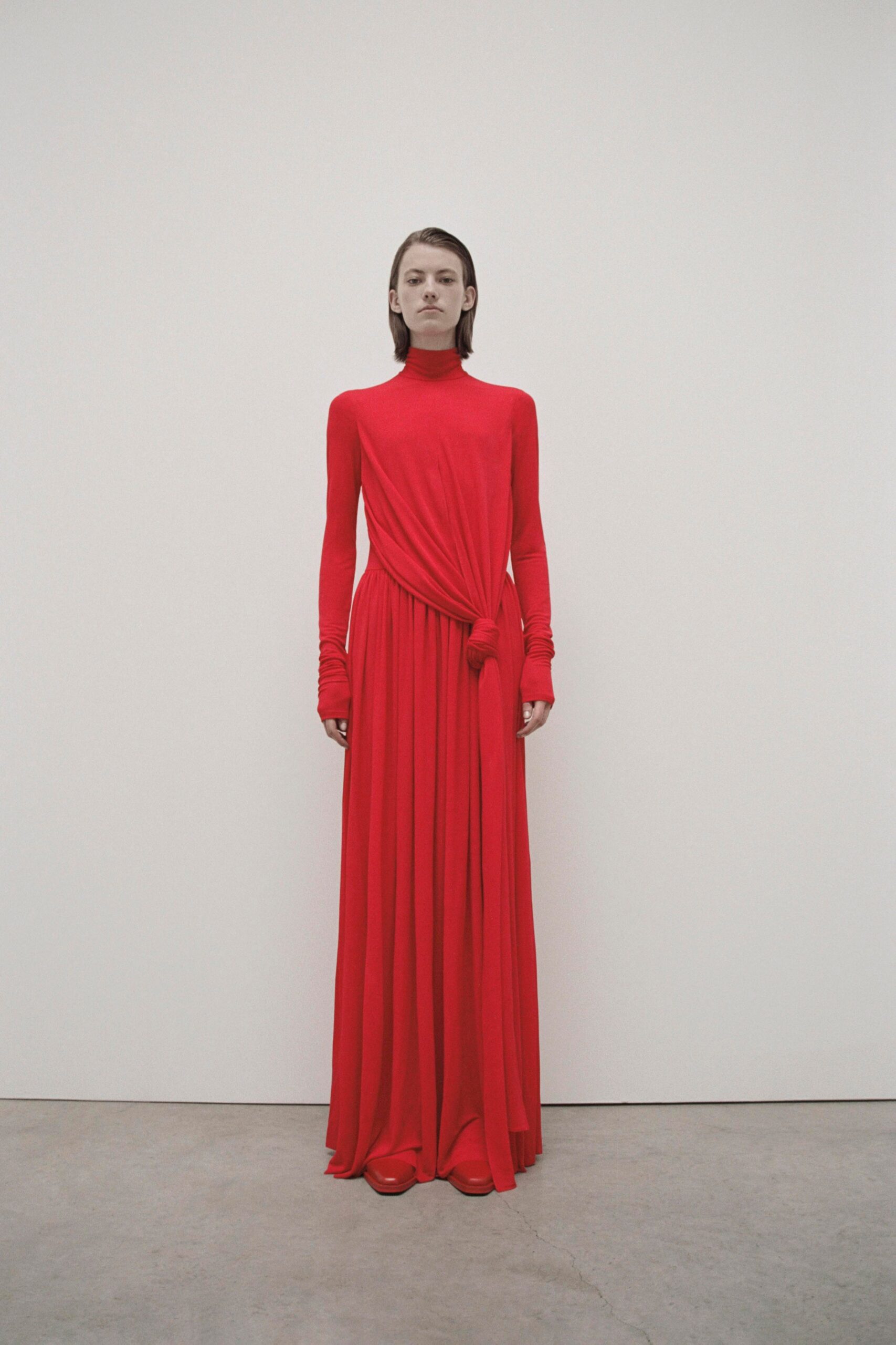 A fitted red silk gown with long sleeves, a high neckline, and draped detailing.
