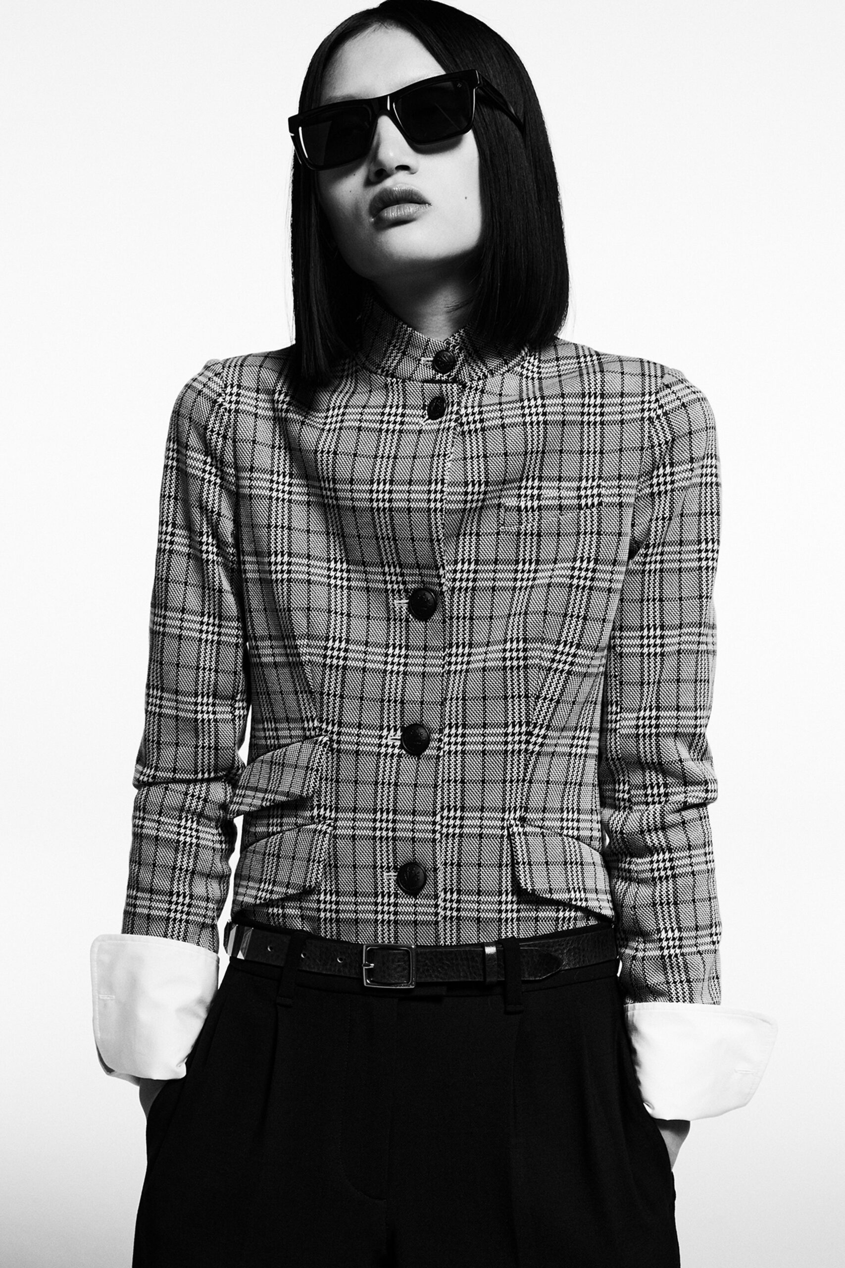 A fitted checked jacket with long sleeves paired with black pants, creating a stylish monochrome look.
