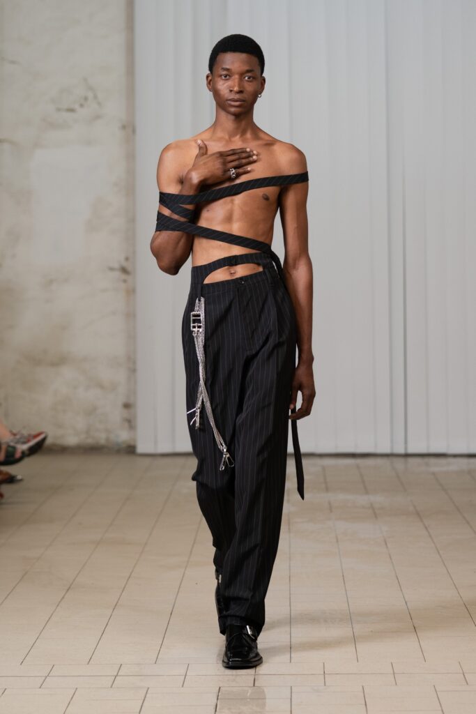 An asymmetric black sleeveless top paired with black pants featuring unique detailing.