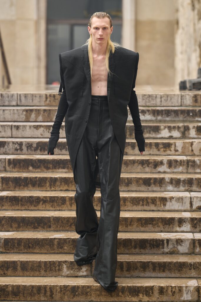 A structured black jacket with long sleeves and asymmetric design paired with matching pants.