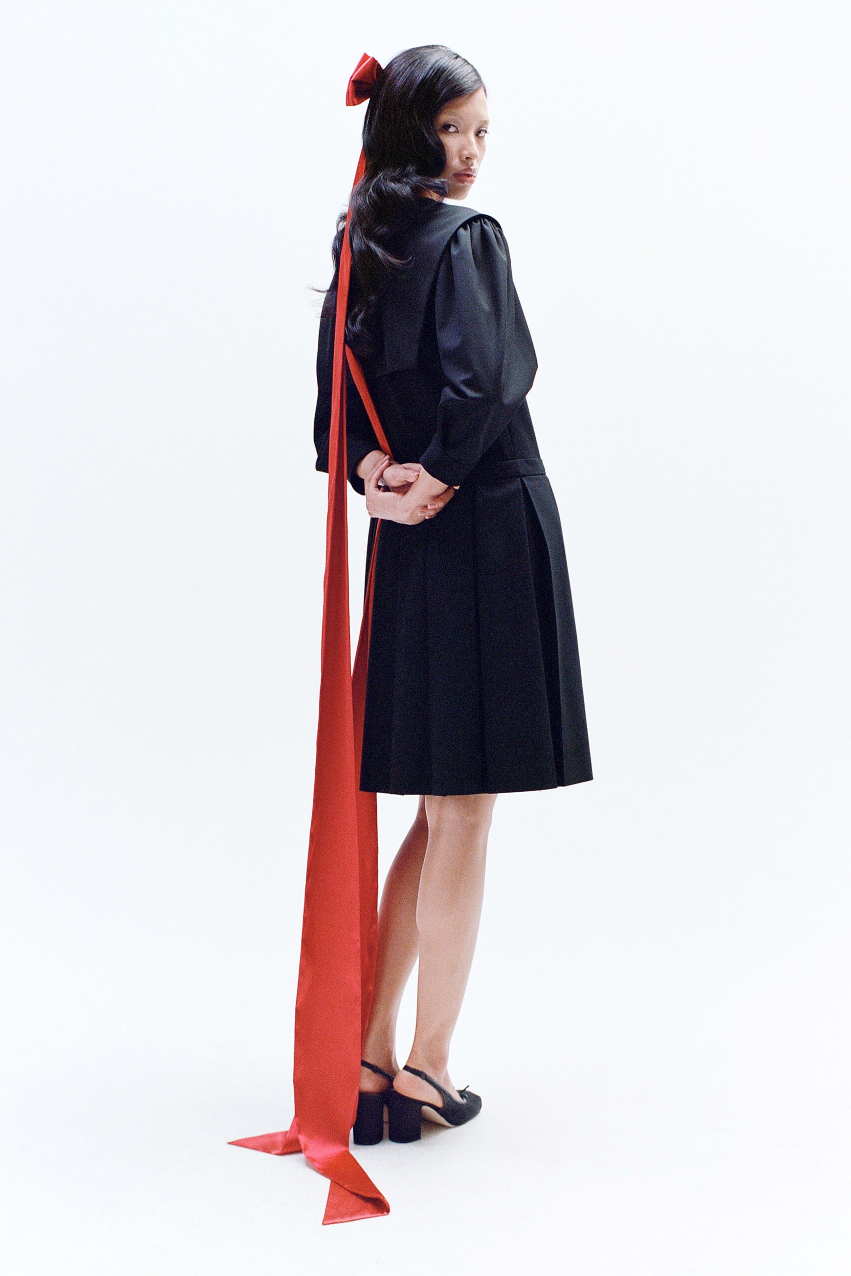 A fitted black dress with long sleeves, a collared neckline, and pleated design details.