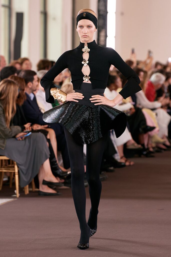 A fitted black silk long-sleeve top with a high neck and an asymmetric pleated skirt.