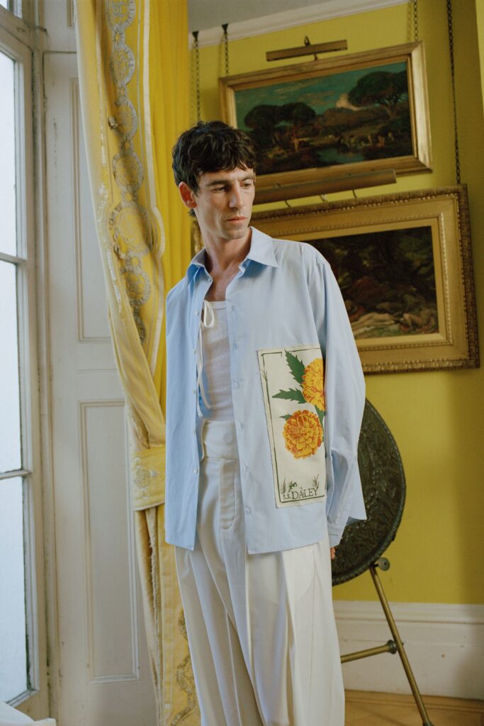 A relaxed blue cotton shirt with long sleeves and a printed detail, paired with white pants.