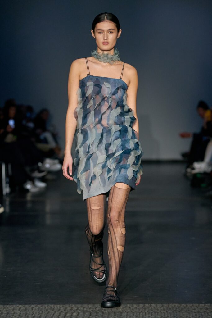 A fitted blue silk sleeveless dress with a V-neckline and asymmetric design.