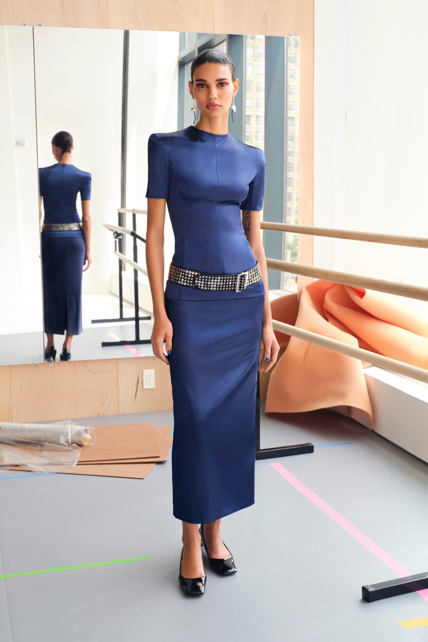 A fitted blue silk dress with short sleeves and a high neckline in a pencil silhouette.
