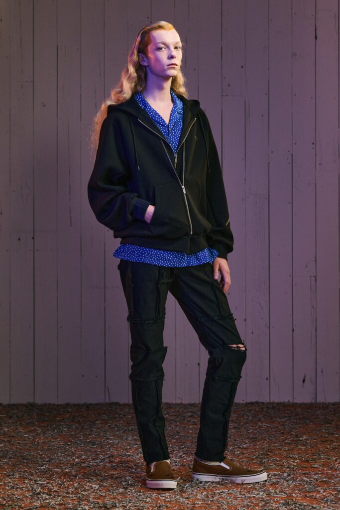 A relaxed black hoodie layered over a blue collared shirt and paired with straight-leg pants.