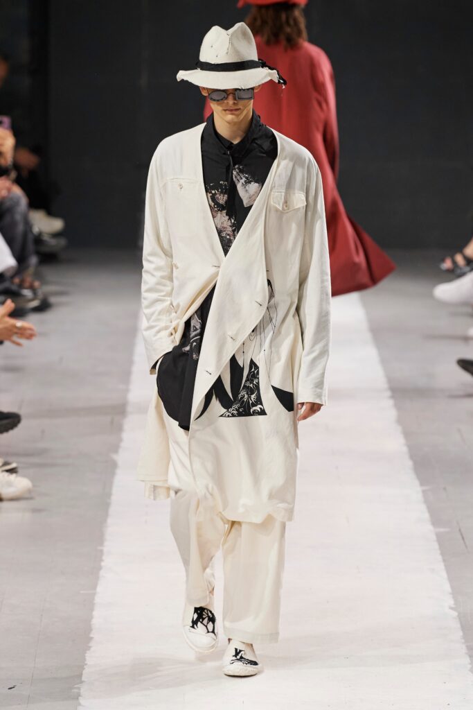 A relaxed white jacket with long sleeves and asymmetric design paired with black pants.