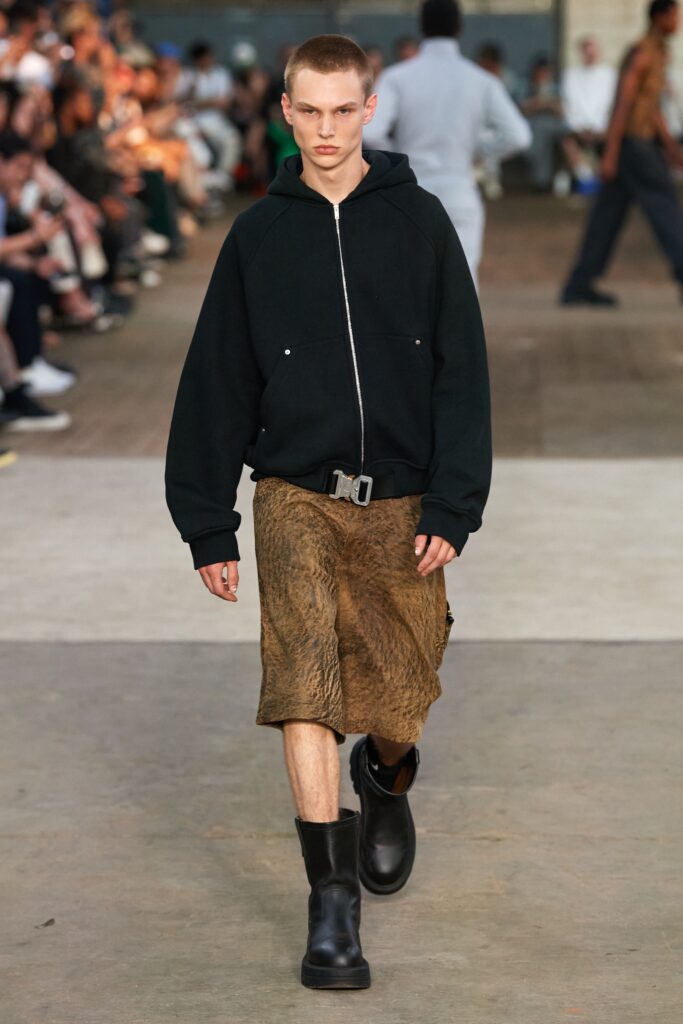 A relaxed black hoodie paired with an asymmetric brown leather skirt.