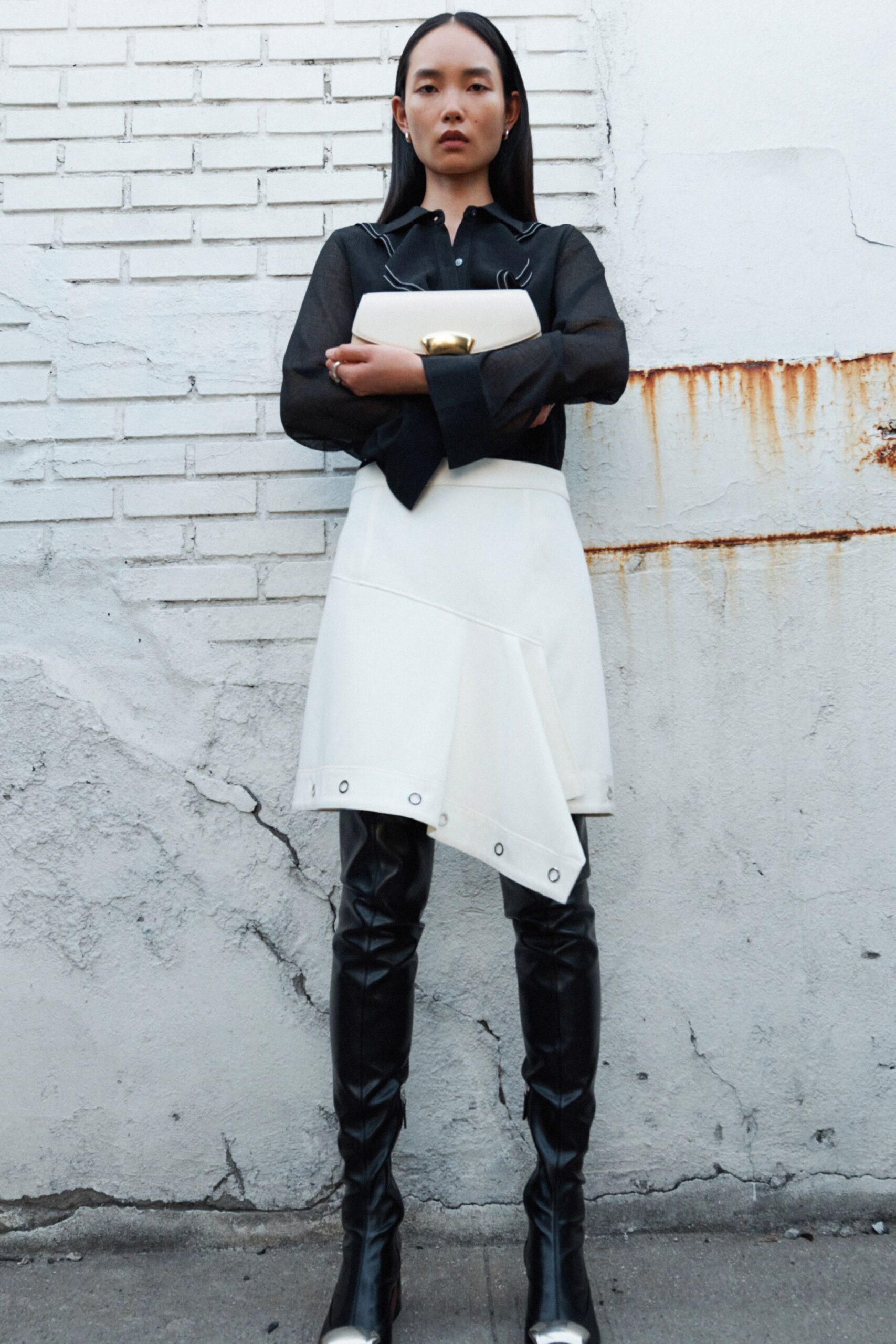 A fitted black leather long-sleeve top with a collared design paired with an asymmetric white skirt.