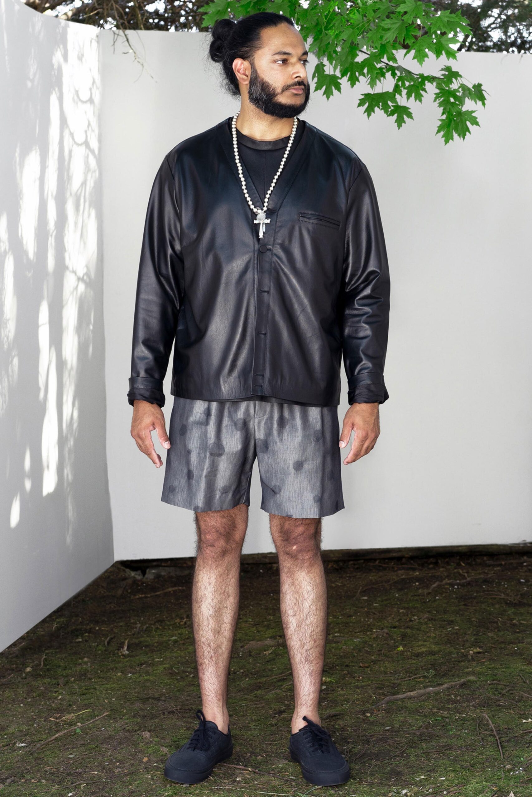 A relaxed black leather jacket with a collared design paired with printed gray shorts.