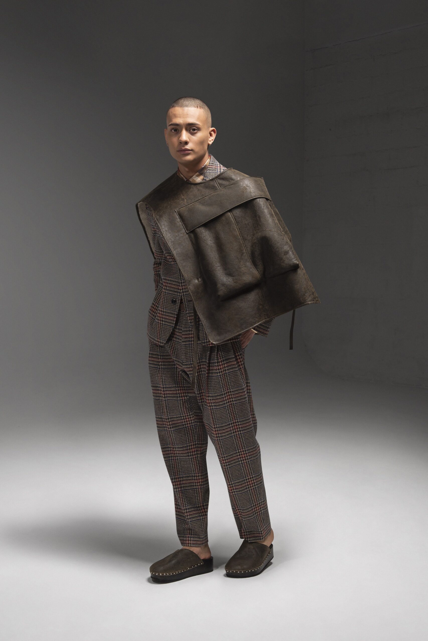 A tailored brown checked suit paired with matching pants and a leather accessory.