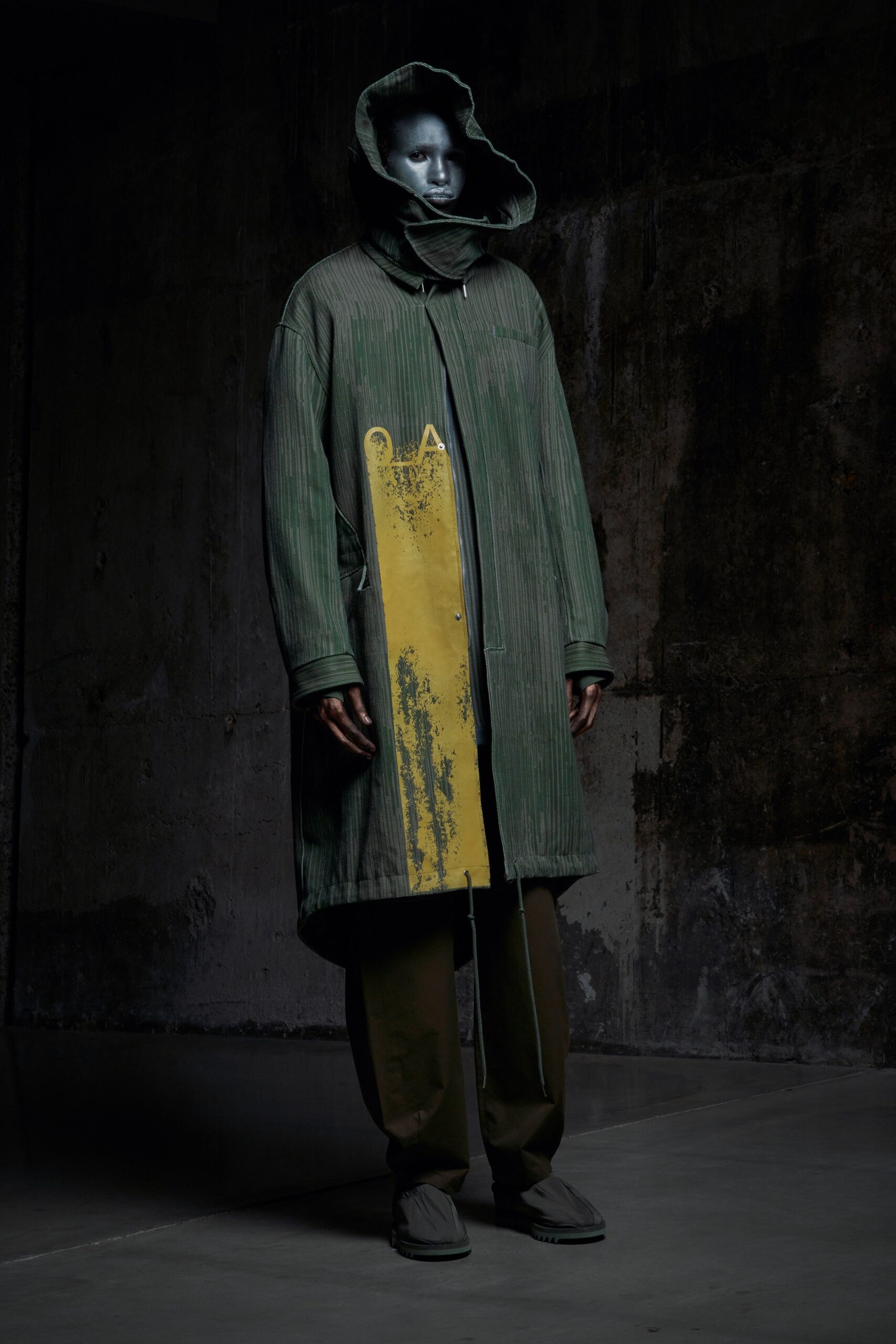 A relaxed green coat with a hood and asymmetric design detail, paired with matching pants.