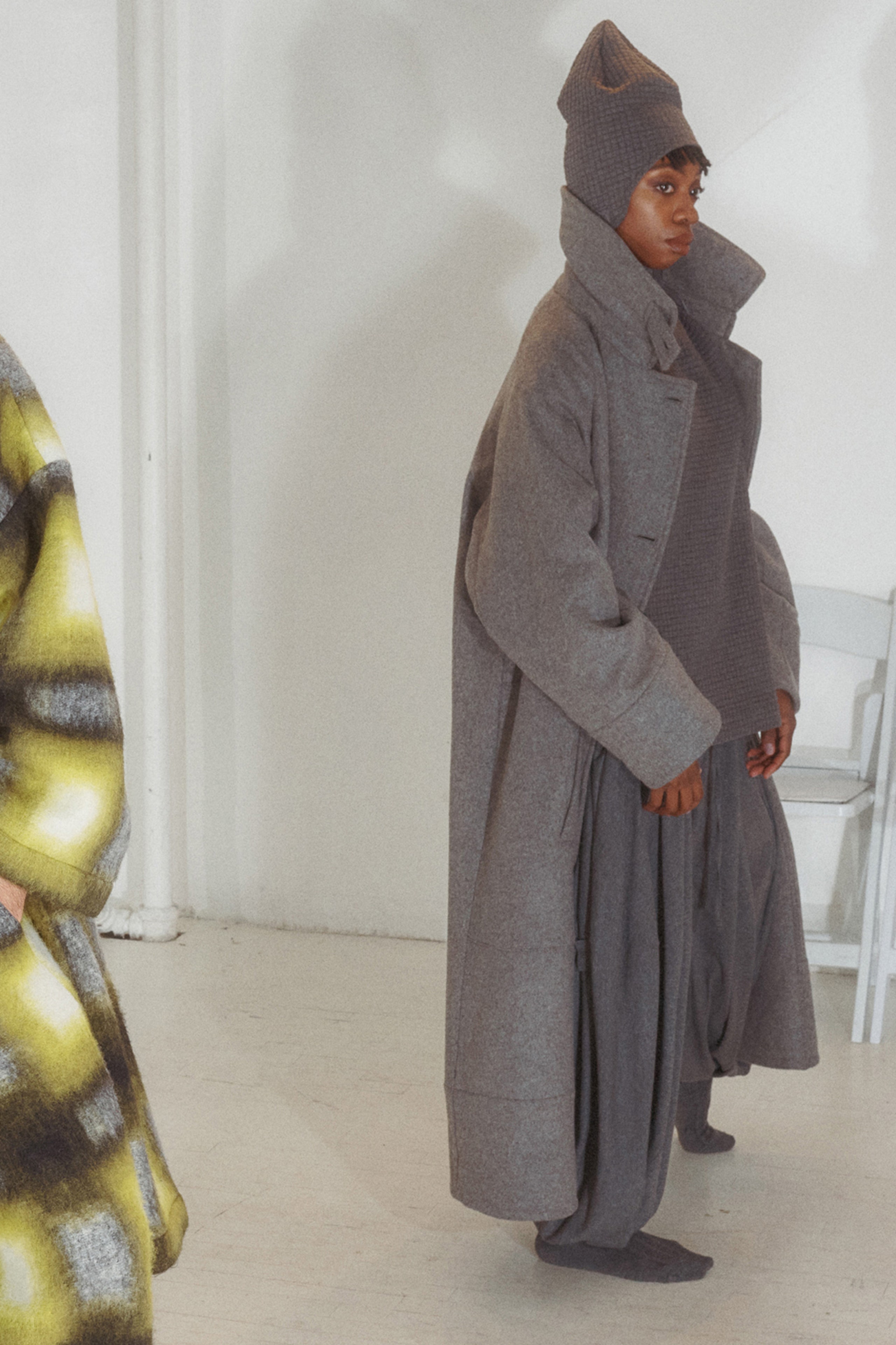 An oversized coat in gray wool, featuring a structured collar and long sleeves that envelop the wearer in warmth. The layered silhouette creates a sense of depth, while the soft texture adds a tactile element to the overall look.