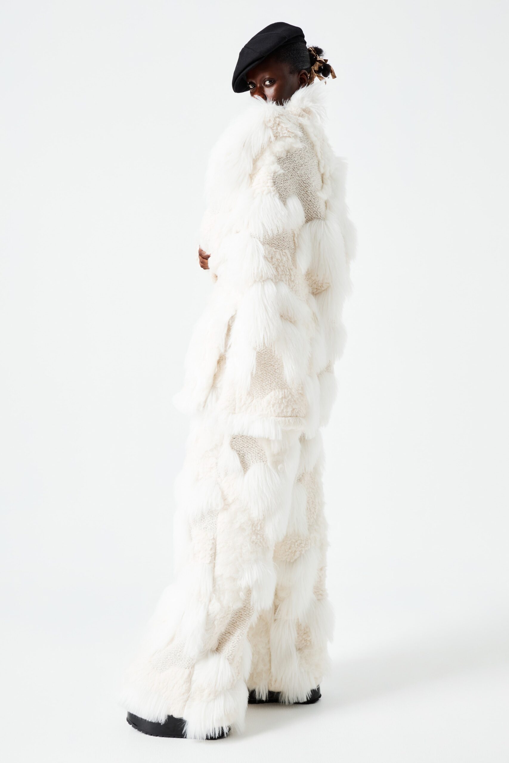 This relaxed jumpsuit showcases a striking silhouette, crafted from plush white faux-fur that adds depth and texture. The layered design creates a dynamic visual effect, while the long sleeves enhance its enveloping form, making it a standout piece on the runway.