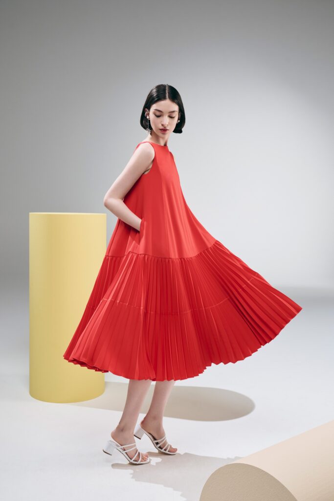 A relaxed red pleated sleeveless dress with a high neckline and tiered design.