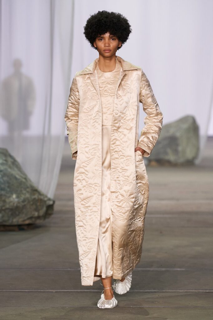 A fitted beige silk coat dress with long sleeves and embroidered detailing.