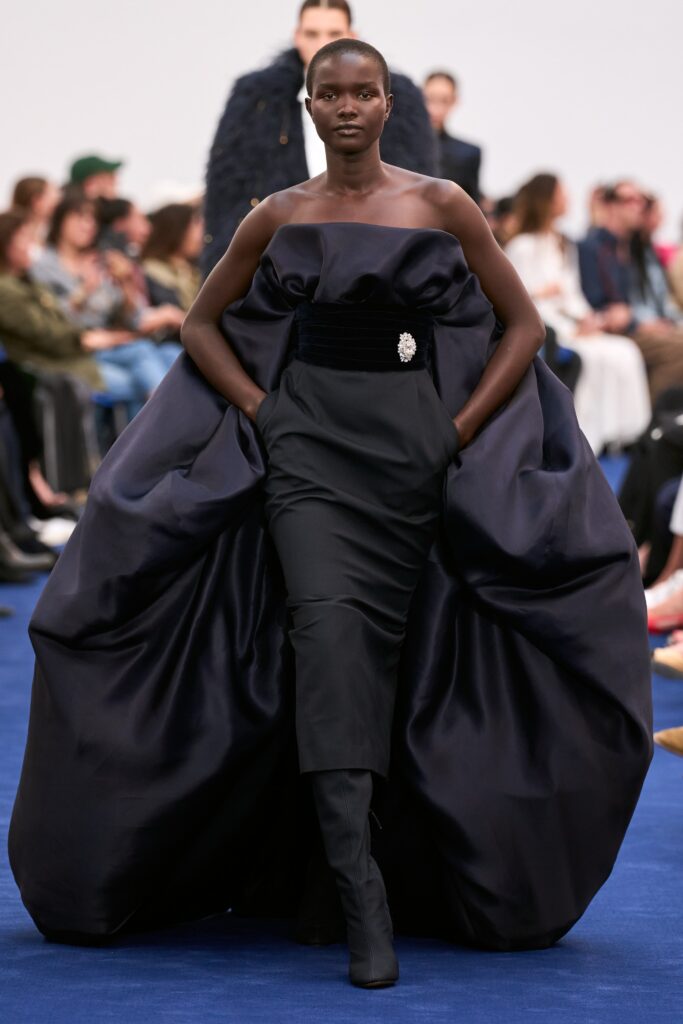 A fitted black silk sleeveless dress with a high neckline and asymmetric design.