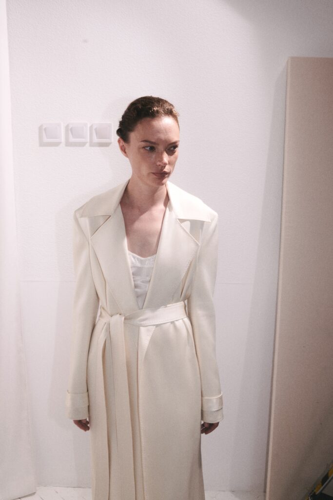 A fitted white silk coat with long sleeves and a belted design detail.