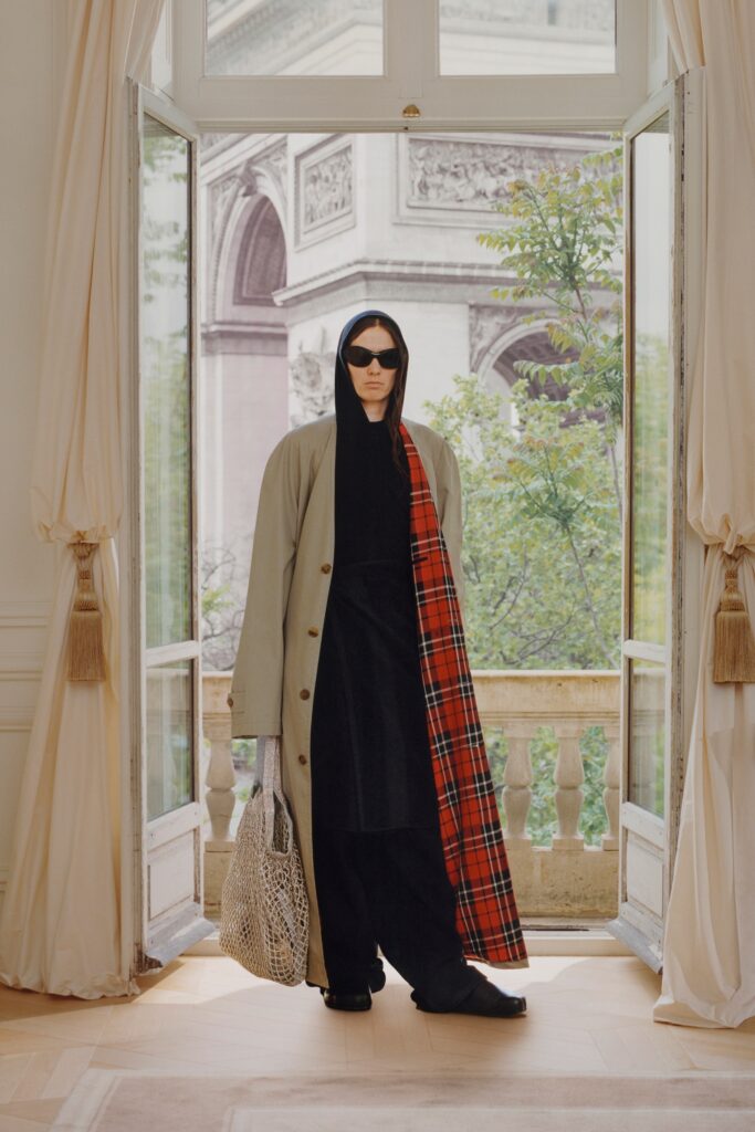 A relaxed beige coat layered over black pants, featuring a hood and plaid detailing.
