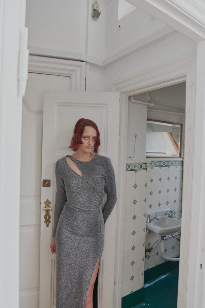 A fitted gray metallic dress with long sleeves, a V-neckline, and a side slit.