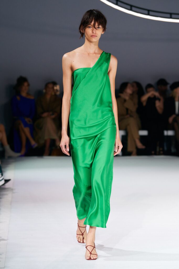 A fitted green silk dress with an asymmetric design and sleeveless construction.