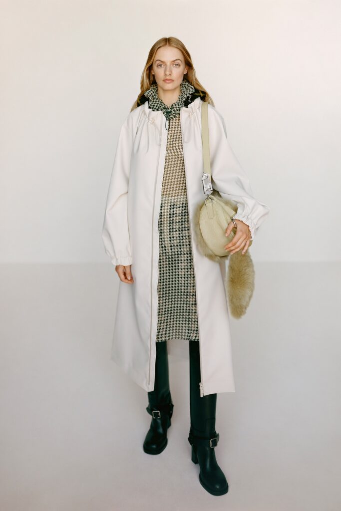 A relaxed white coat worn over a checked dress with long sleeves and a collared neckline.