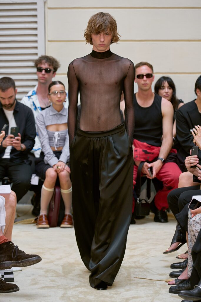 A relaxed black sheer long-sleeve top paired with wide-leg silk pants.