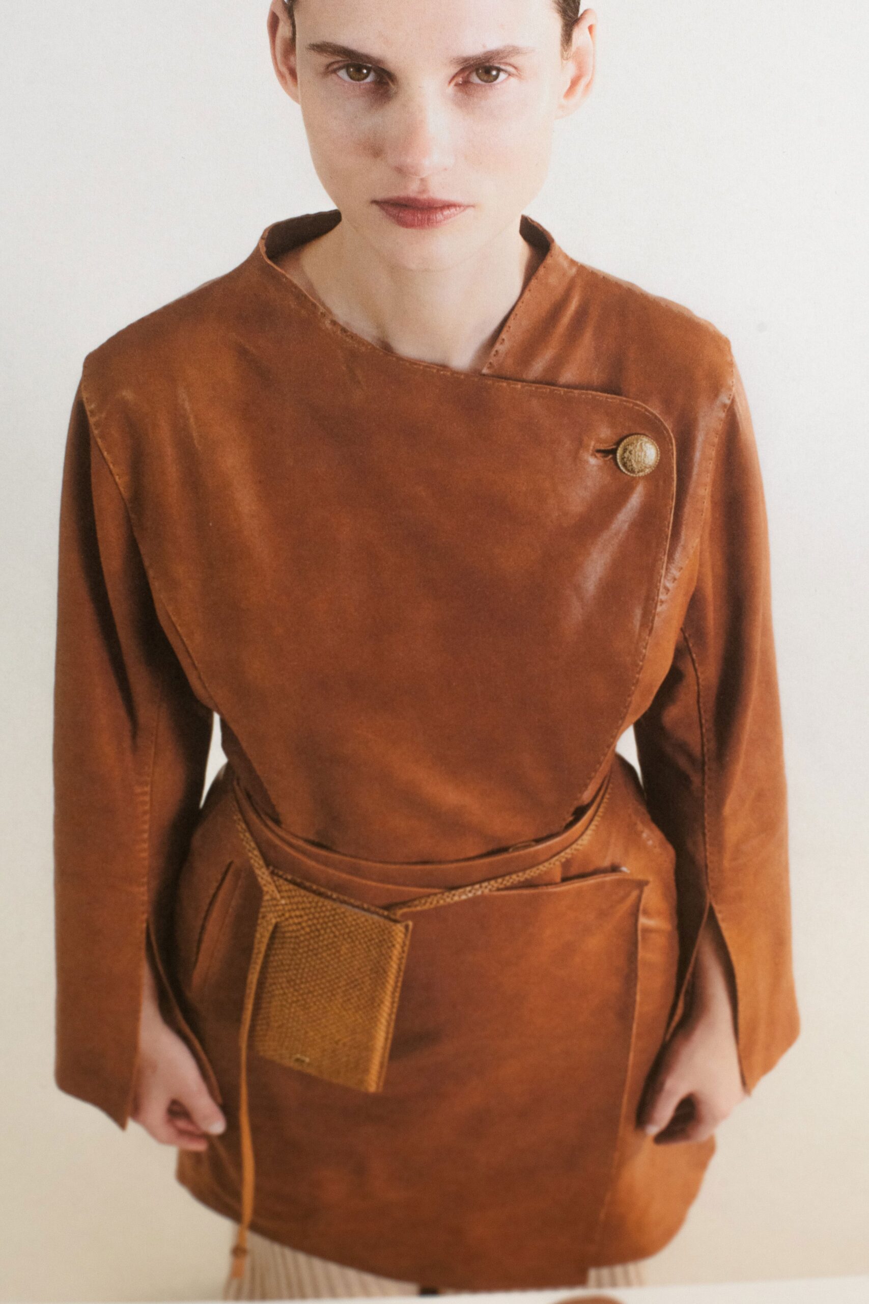 A fitted brown leather dress with long sleeves and an asymmetric design detail.