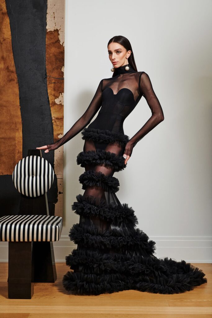 A fitted black silk dress with long sleeves, a V-neckline, and ruffled detailing.