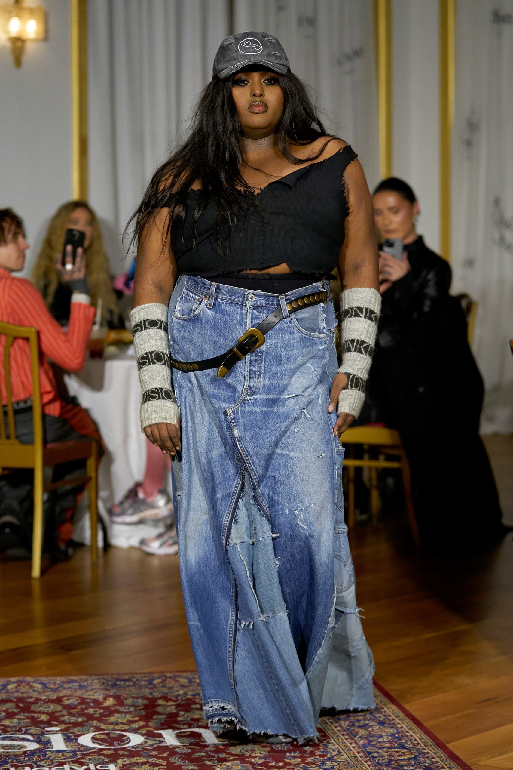 A relaxed black sleeveless top paired with a high-waisted, fringed blue denim skirt.