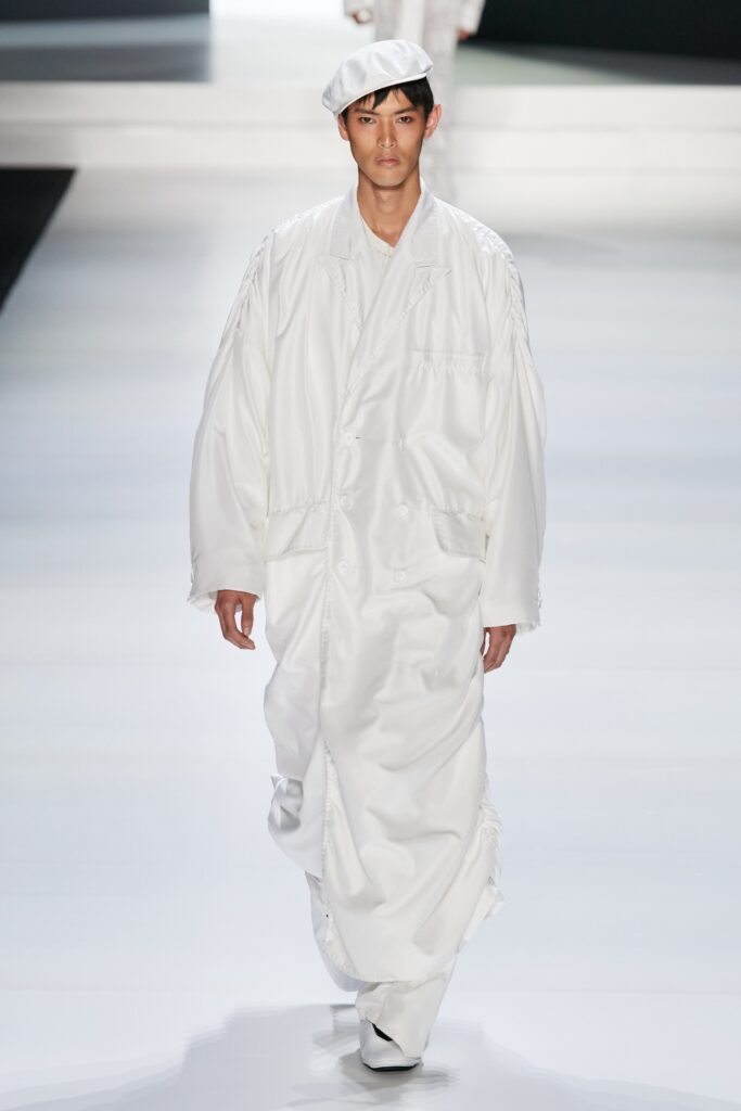 An oversized white silk coat with long sleeves and a collared design, featuring button details.
