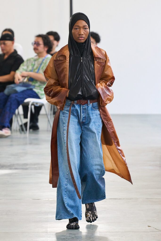A relaxed brown leather coat layered over a black top and wide-leg blue denim pants.