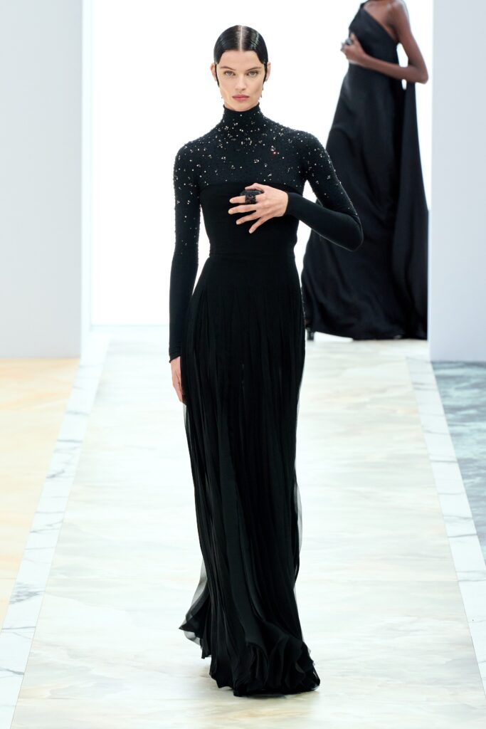 A fitted black silk gown with long sleeves, a high neckline, and pleated detailing.