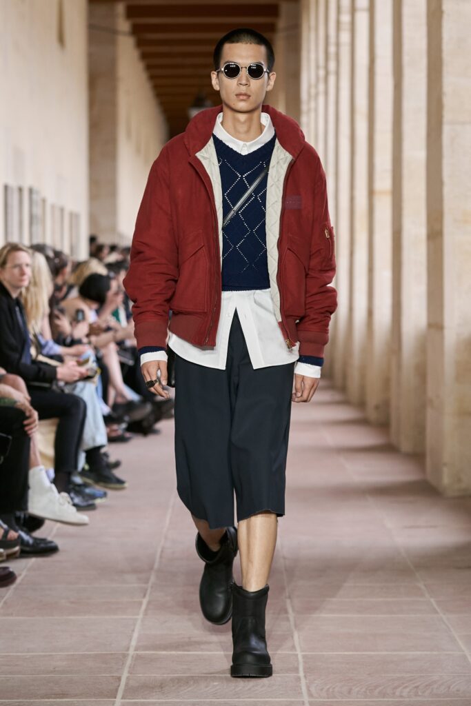 A relaxed fit red jacket layered over a collared shirt and paired with navy shorts.