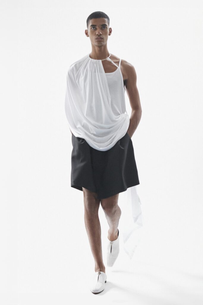 A relaxed white draped sleeveless top paired with black shorts, featuring an asymmetric design.