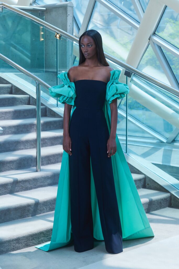 A fitted black jumpsuit paired with an off-shoulder green cape featuring an asymmetric design.