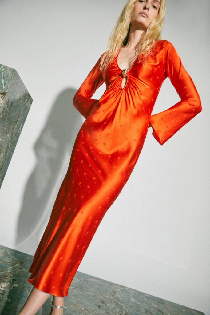 A fitted red silk dress with long sleeves, a V-neckline, and a stylish slit.