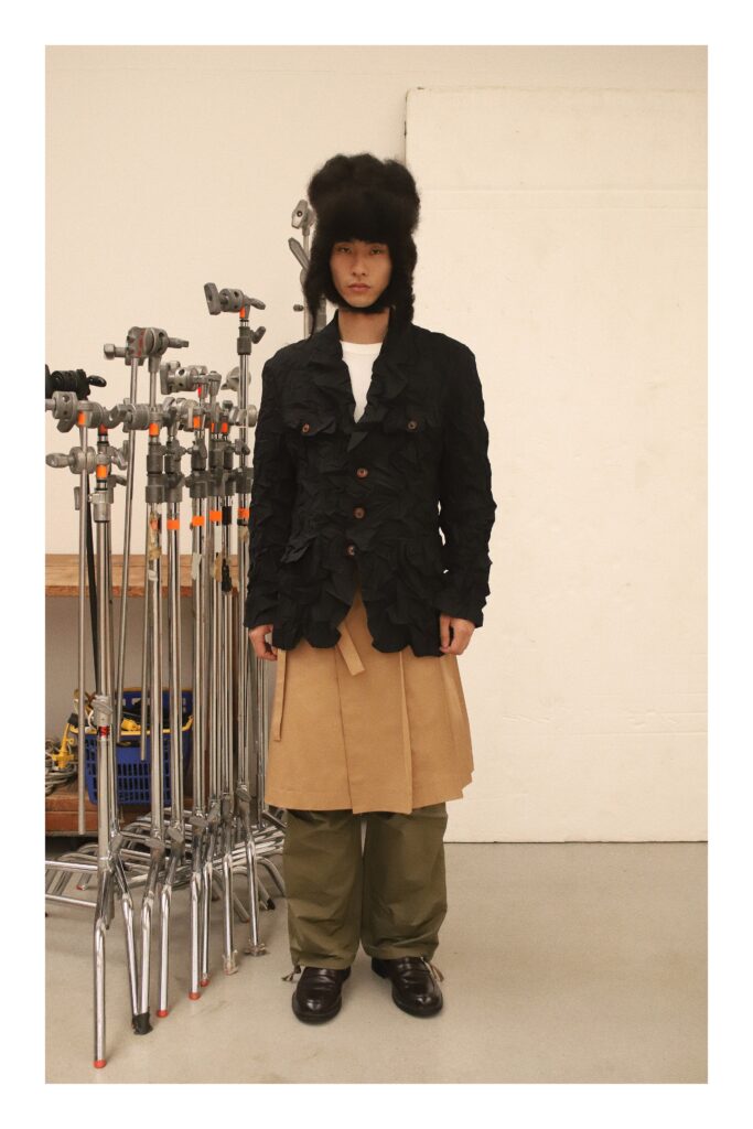 An oversized black layered jacket paired with beige pants and green accents.