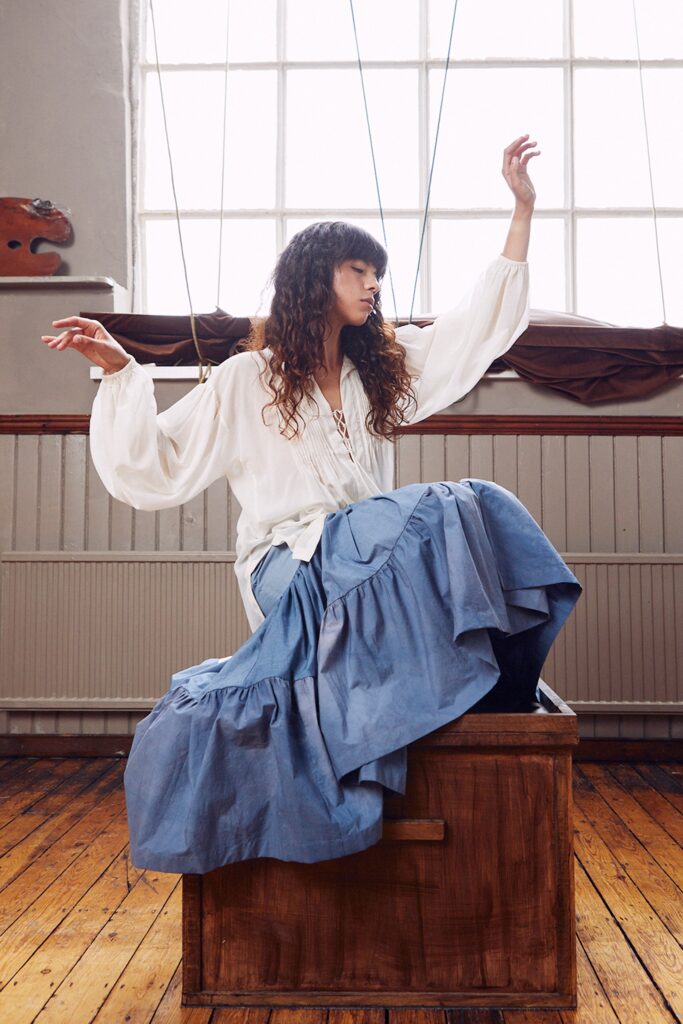 A relaxed white cotton long-sleeve blouse paired with a tiered blue skirt.