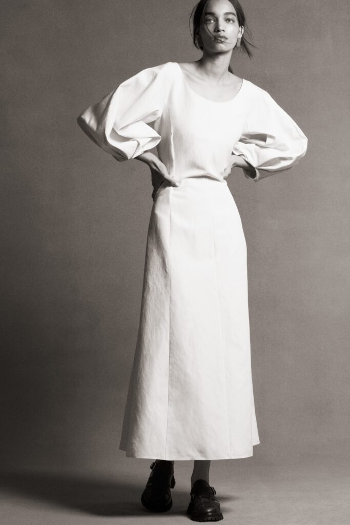 A fitted white cotton dress with long sleeves and a straight-leg silhouette.