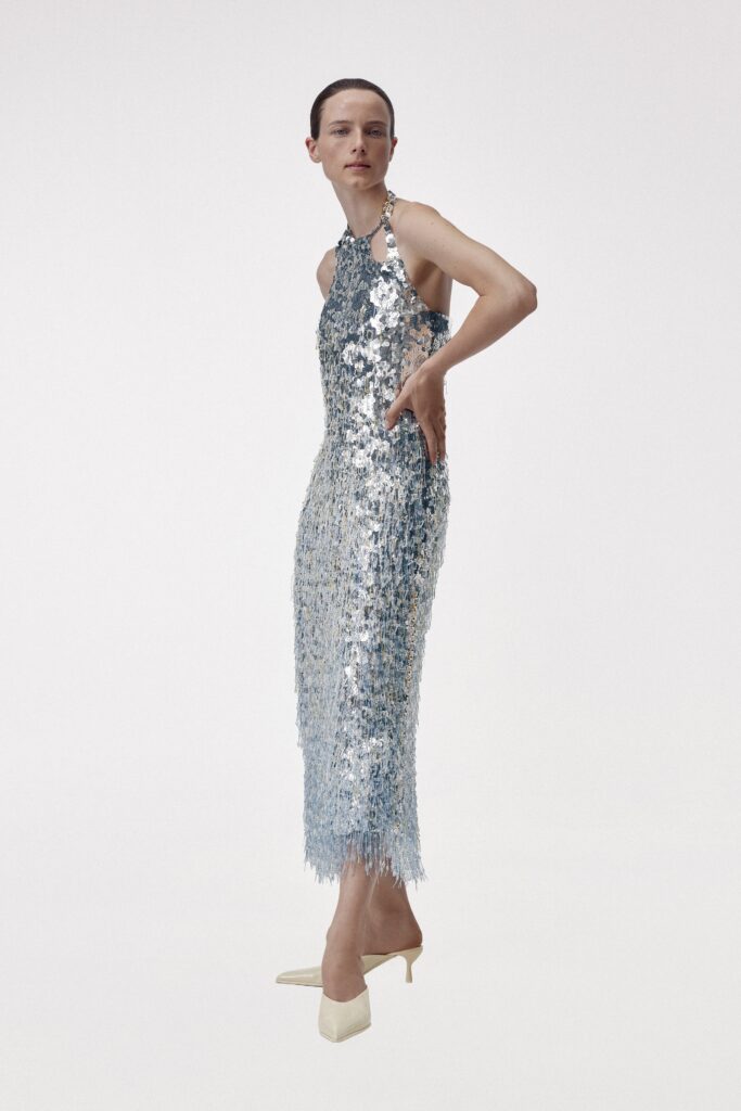 A fitted silver sequin dress with a sleeveless design and high-neck construction featuring a slit.