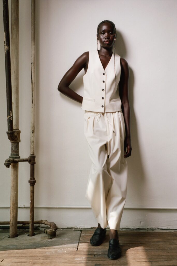 A relaxed beige cotton sleeveless vest paired with pleated pants for a chic look.