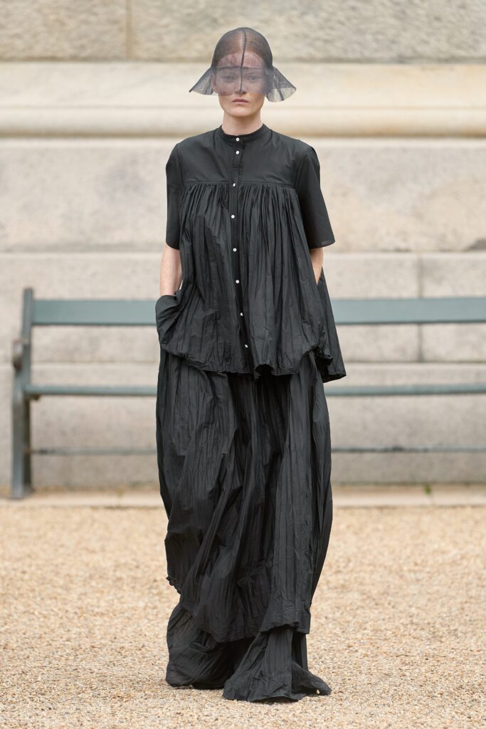 A relaxed black dress with short sleeves, a collared neckline, and pleated design details.