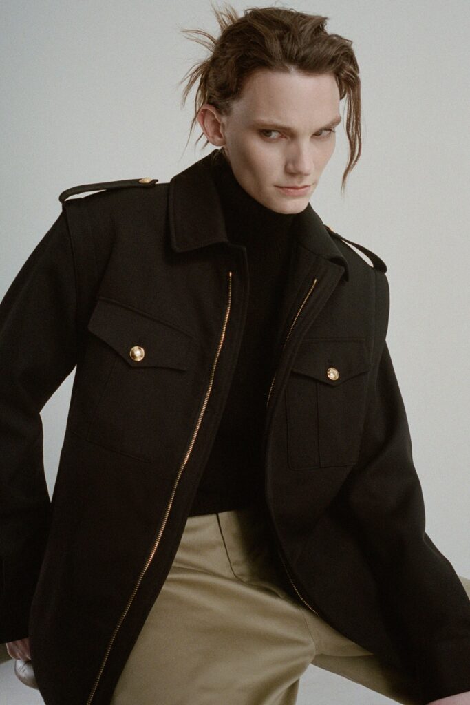 A relaxed black wool jacket with long sleeves and a collared design paired with beige pants.