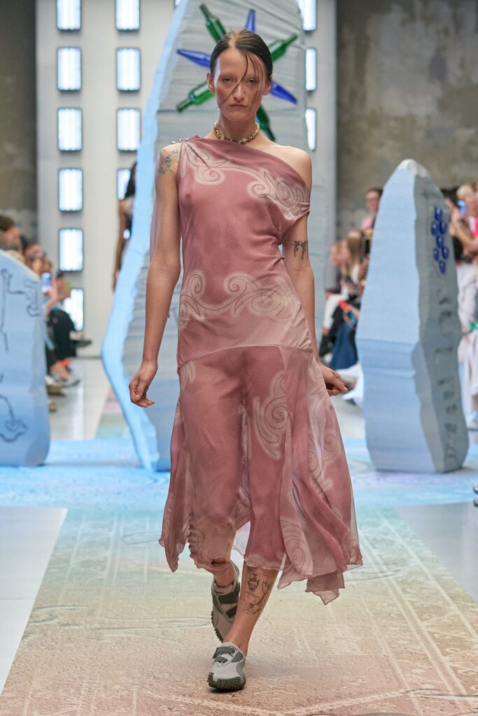 A relaxed pink sheer dress with an asymmetric design and layered details.